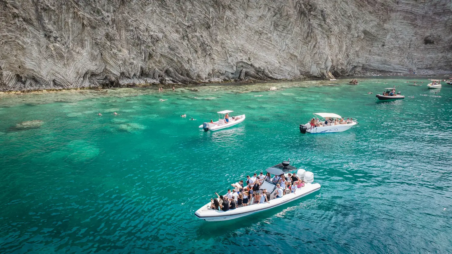 The Beast Boat anchored below white limestone cliffs in a turquoise Albanian Riviera cove