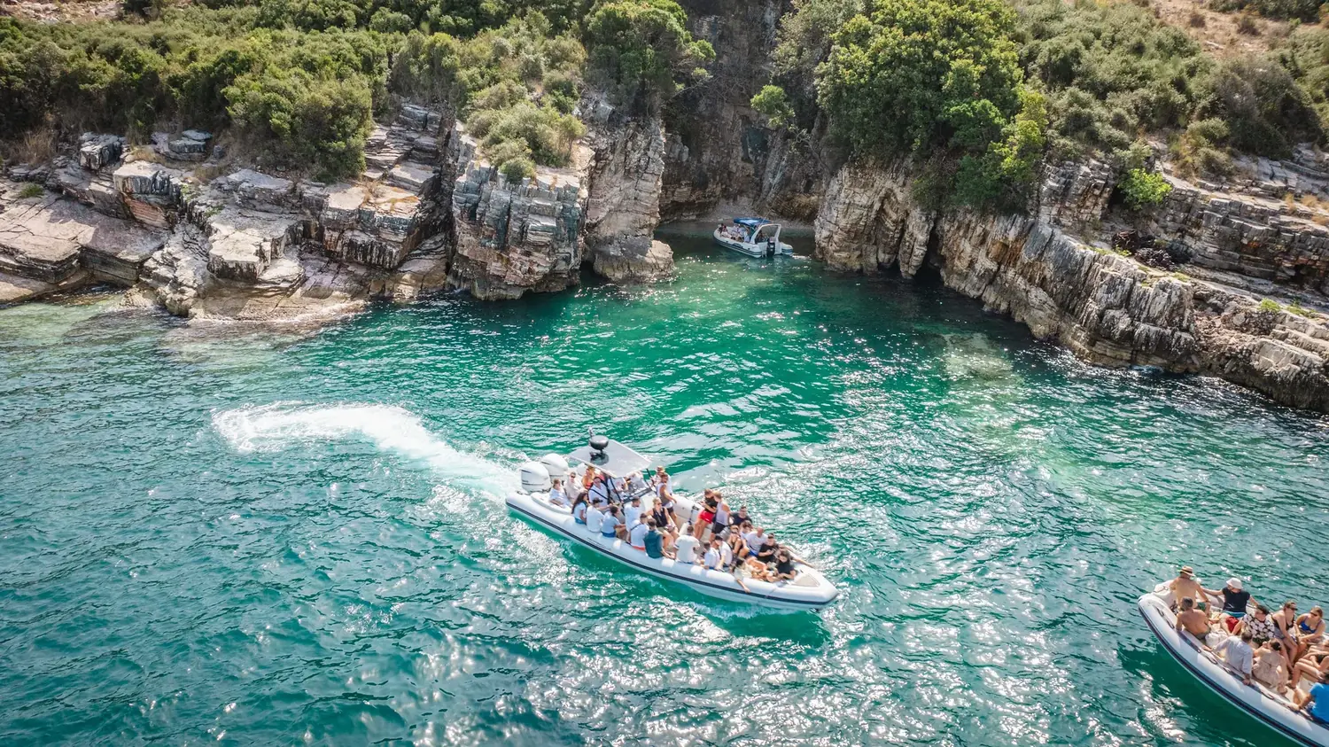 The Beast Boat under way with guests aboard, leaving a wake across a turquoise Saranda cove